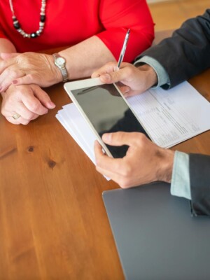 Business meeting at a wooden table with consultant reviewing documents and using a digital tablet.