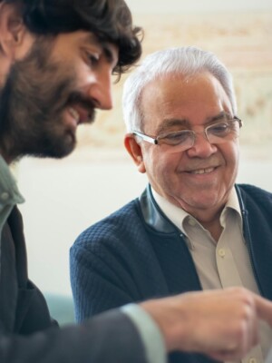 Elderly man discussing business with a younger colleague using a laptop indoors.