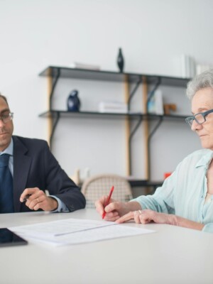Elderly woman signing paperwork in modern office with consultant.